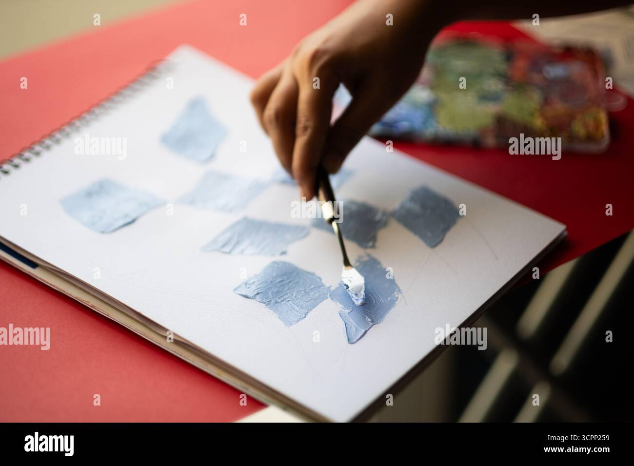 Nahaufnahme des Malers mit einem Palettenmesser, um Farben zu mischen und Farbmuster auf Papier, künstlerische Kreativität und abstrakte Malerei zu kreieren Stockfoto