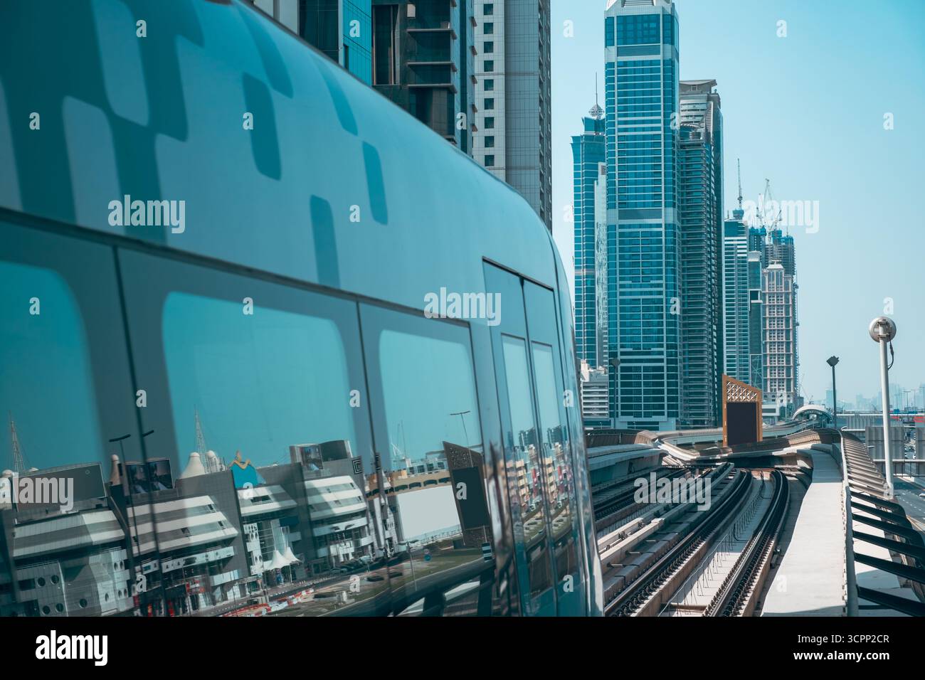 Moderne Glashochhäuser dominieren die Skyline der Stadt und spiegeln den blauen Himmel und einen Zug, der an einer hohen Stahlstation in einer geschäftigen Stadt wie Shanghai vorbeifährt Stockfoto