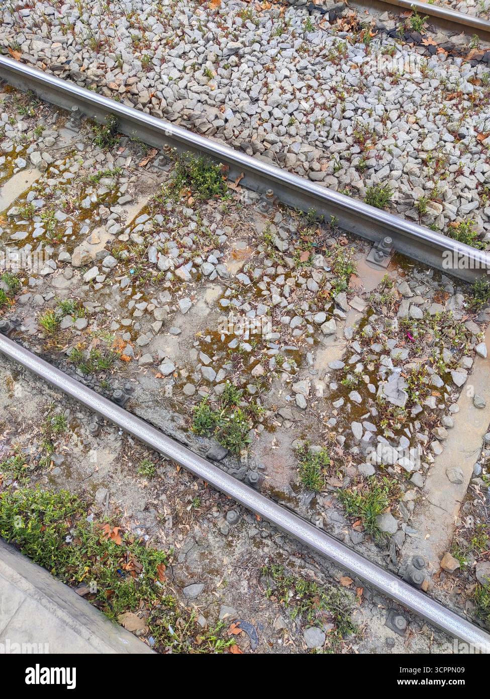 Eine Nahaufnahme alter Eisenbahngleise mit verstreutem Kies und Grasflecken, die zwischen den Schwellen wachsen. Ideal für den Transport. Stockfoto