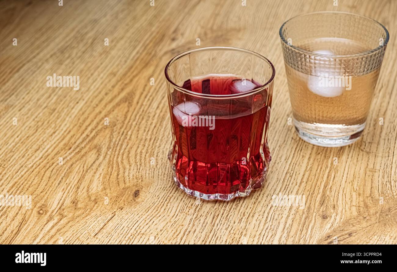 Erfrischende Getränke mit Eis. Zwei Gläser, eines mit einem roten Getränk und Eiswürfeln gefüllt, das andere mit einer klaren Flüssigkeit und Eis. Stockfoto