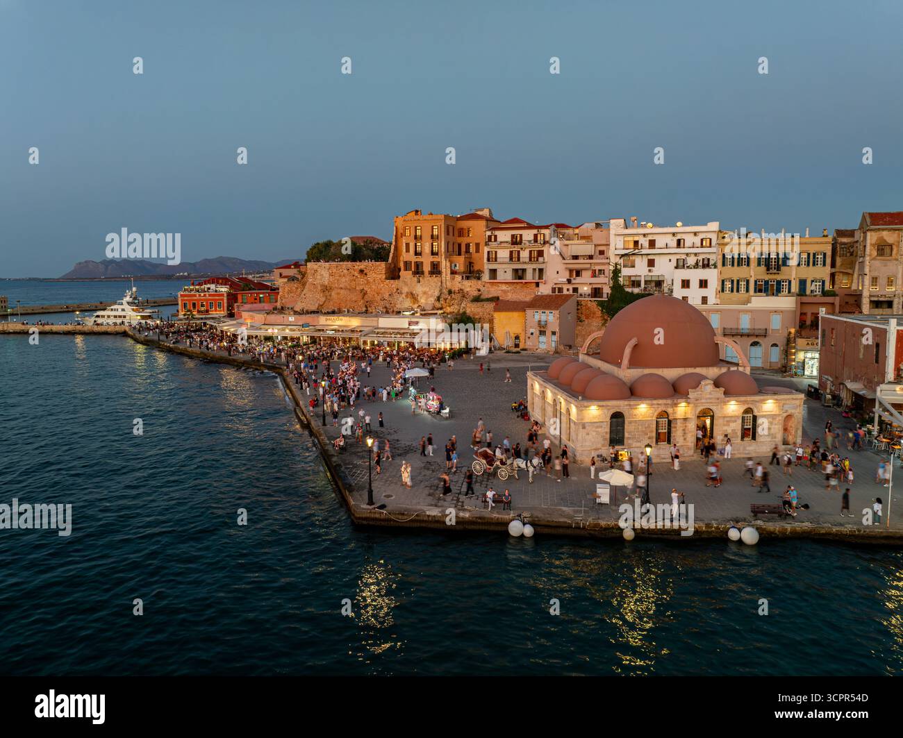 Aus der Vogelperspektive der Kioutsouk Hassan Moschee mit ihrer markanten Kuppel leuchtet warm inmitten des geschäftigen Hafens, ein lebhafter Kontrast zum tiefblauen Meer, Chania, Chania, Griechenland. Stockfoto