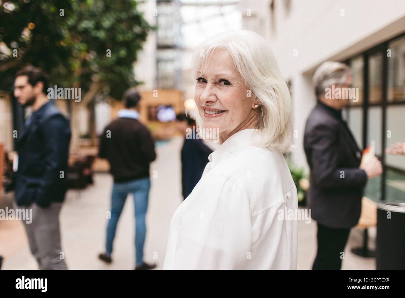 Porträt einer lächelnden Geschäftsexpertin mit weißem Haar, das über die Schulter schaut Stockfoto