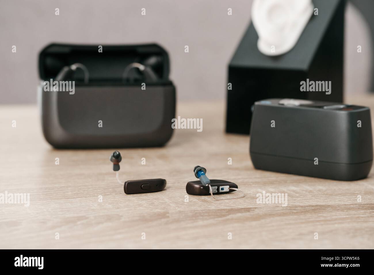 Moderne digitale Hörgeräte mit Ladetasche auf Holztisch in der audiologischen Klinik. Hörgerät, Ladegerät und Ohrmodell zur Anbringung und Demonstration. Stockfoto