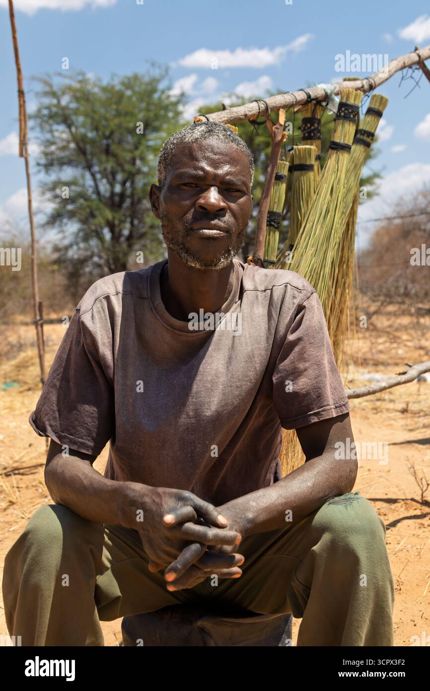 Einzelner afrikanischer Mann, Dorf, Straßenverkäufer, der Besen am Straßenrand verkauft Stockfoto