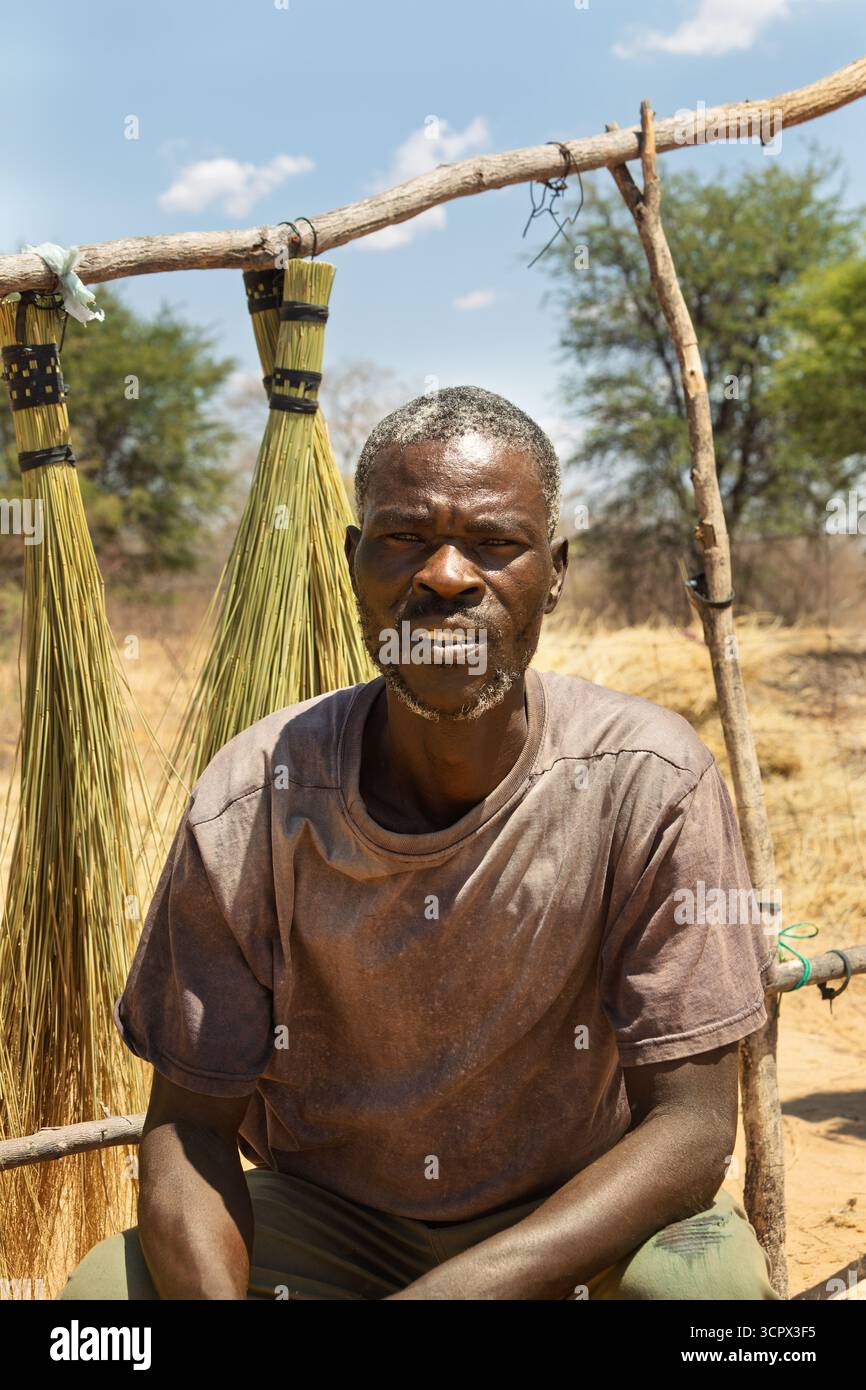 Einzelner afrikanischer Mann, Dorf, Straßenverkäufer, der Besen am Straßenrand verkauft Stockfoto