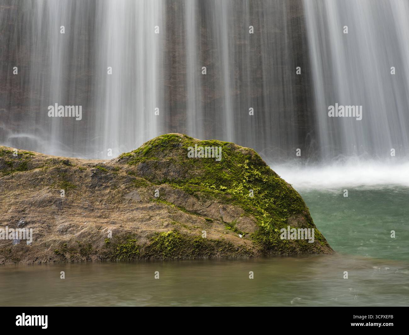 Nahaufnahme von Waterfall Cascading Down Rocks – vertikale Aufnahme mit Langzeitbelichtung, um einen seidenweichen, glatten Effekt von Wasser zu erzeugen, das über strukturierte, rote Flecken strömt Stockfoto
