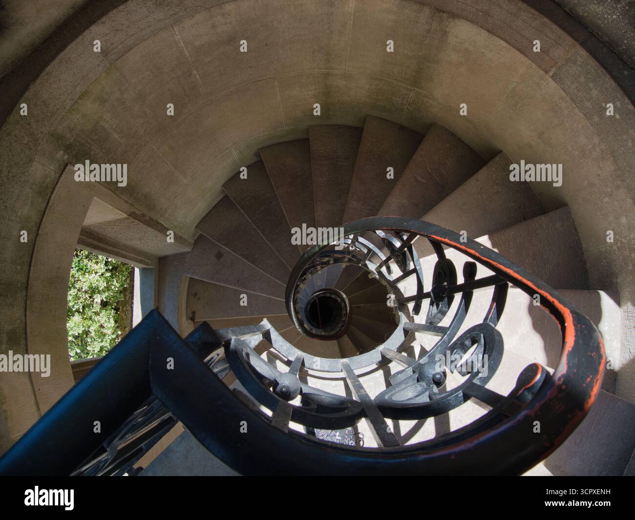 Architektonische Wendeltreppe mit Blick nach unten - beeindruckender Blick über die Höhe einer historischen Wendeltreppe aus Stein mit dunklem schmiedeeisernem Geländer, der d Stockfoto