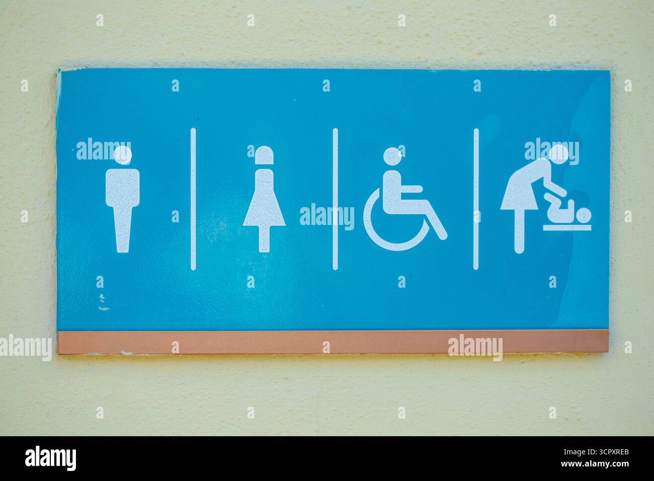 Ein blaues Schild für die Toilette mit weißen Figuren, die den Zugang für Männer, Frauen, Behinderte und die Wickelmöglichkeiten für Babys an einer gelb strukturierten Wand anzeigen. Stockfoto