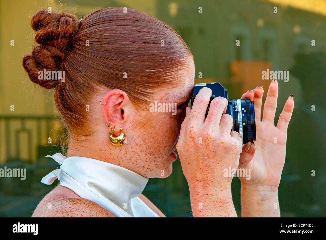 Ein cooles, schönes rothaariges Mädchen mit Sommersprossen macht ein Foto mit einer Anlog-Kamera Stockfoto