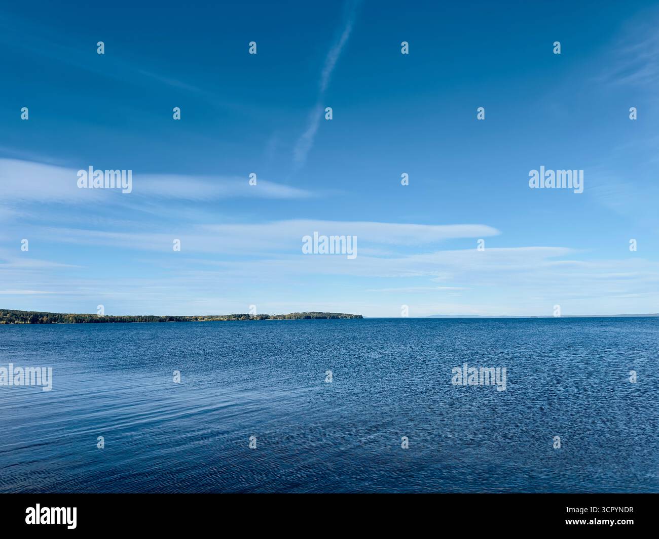 Ruhiger Blick auf den See unter einem hellblauen Himmel mit schimmernden Wolken. Stockfoto