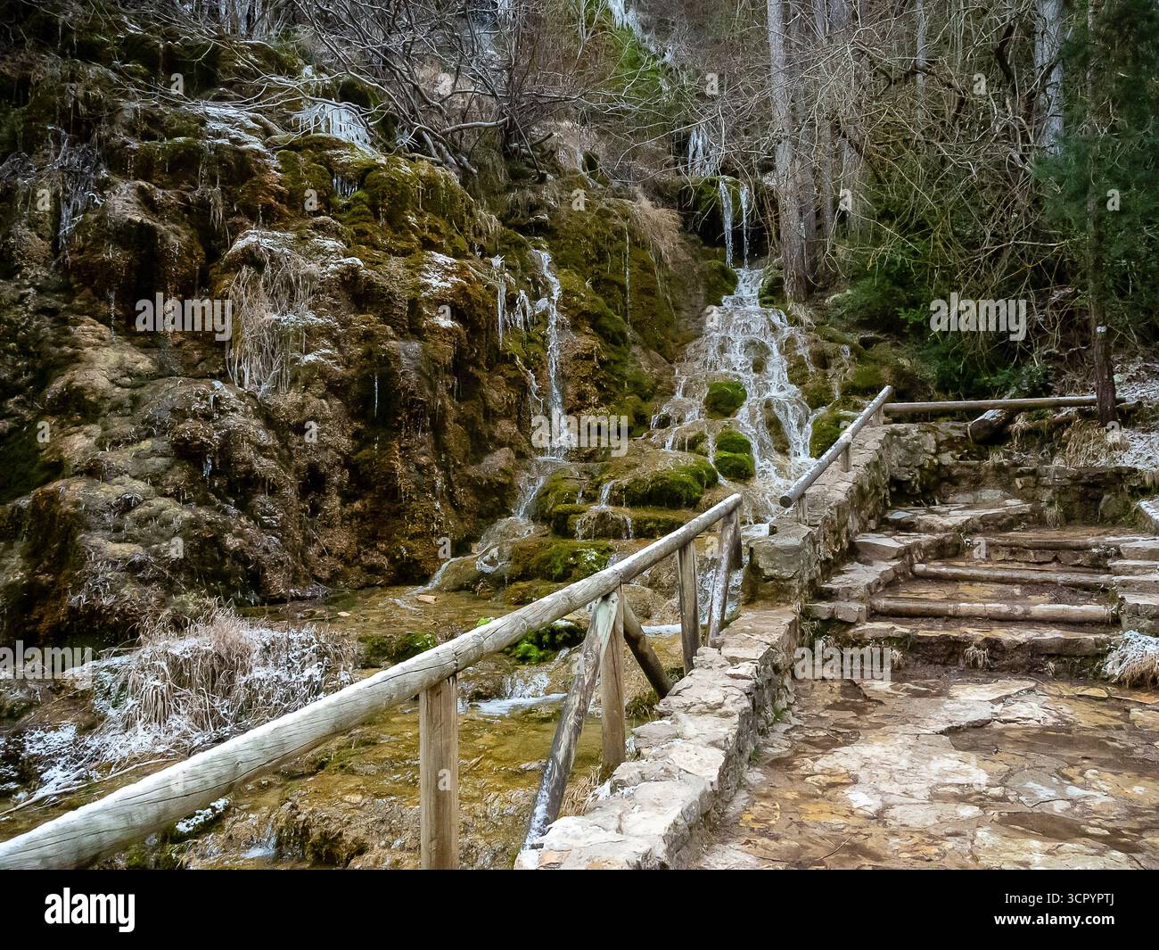 Ein wunderschöner Wasserfall fließt durch moosbedeckte Felsen neben einem rustikalen Holzsteg in einem ruhigen Waldgebiet. Stockfoto