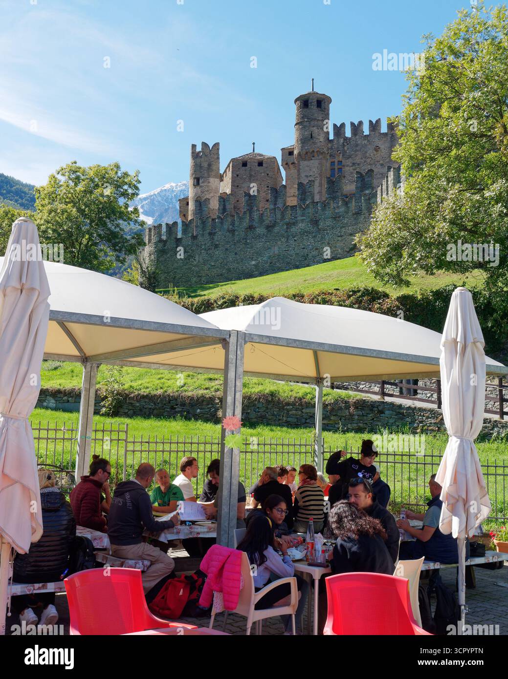Fenis Castle, ein historisches Wahrzeichen und Museum in der Stadt Fenis mit Leuten in einem Restaurant im Vordergrund. Aosta Valley, NW Italien. September 2025. Stockfoto