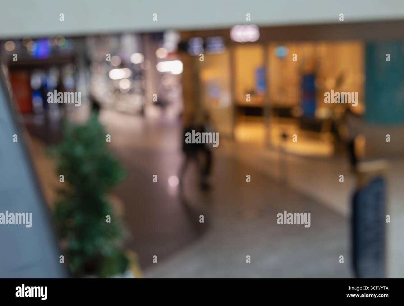 Abstrakter Blick nach unten auf einen verschwommenen Gang des Einkaufszentrums mit einer Figur, die an einem kleinen Topfbaum vorbeigeht und urbanes Leben, Handel und Bewegung vermittelt Stockfoto