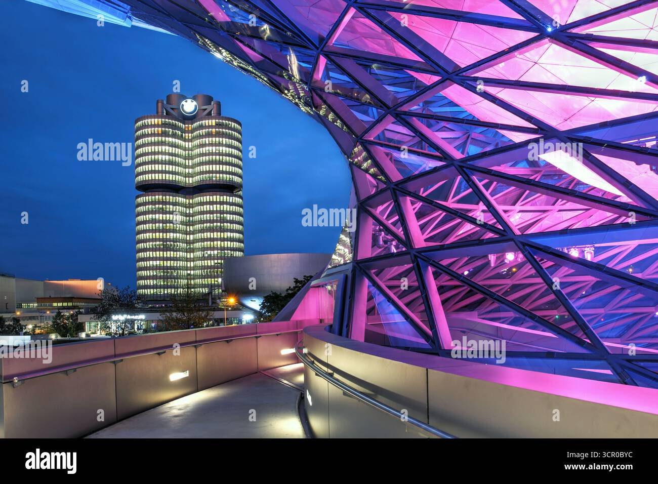 Nachtszene mit BMW Tower, dem Hauptquartier des Automobilriesen, der durch die Bögen der jüngeren BMW Welt gesehen wird, einem Showroom und einem Geschäft für t Stockfoto