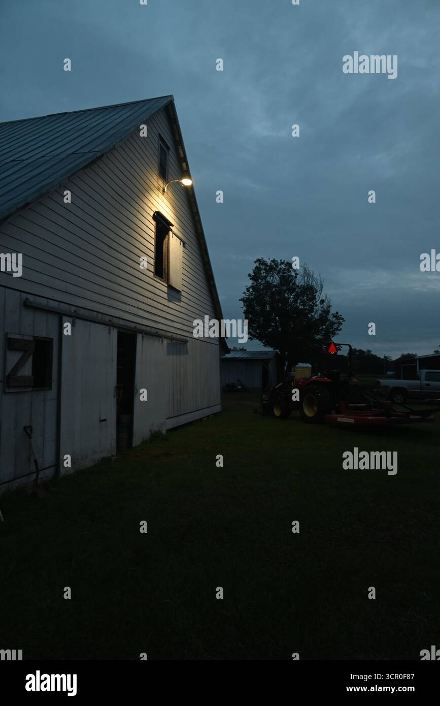 Eine Jahrhunderte alte weiße Scheune wird in den frühen Morgenstunden von einem einsamen Licht beleuchtet. Stockfoto