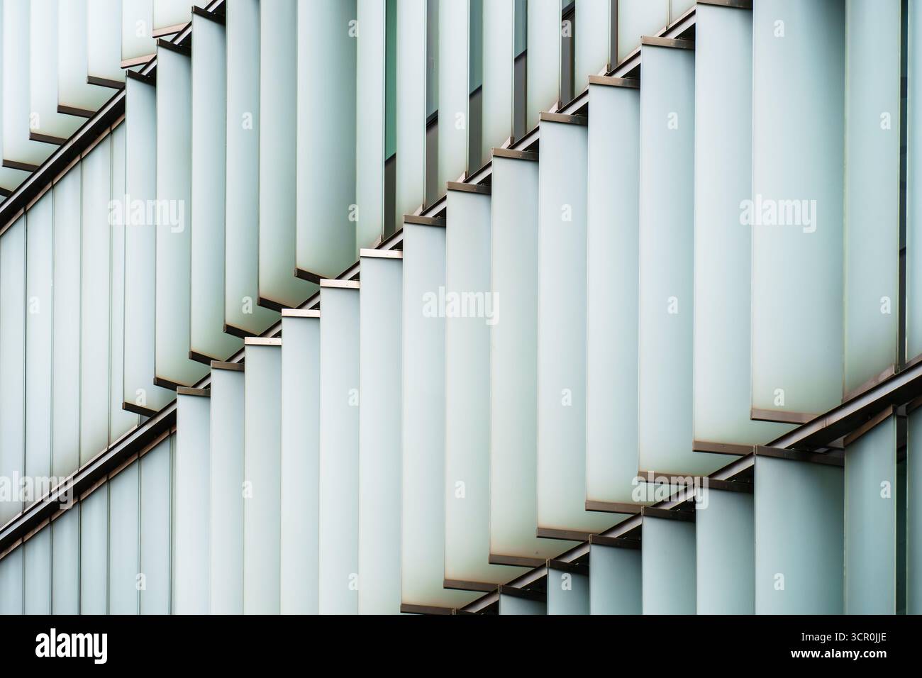 Abstrakte Fassade mit gestaffelten Milchglaspaneelen, die rhythmisch geometrische Schichten aus Licht und Schatten bilden Stockfoto