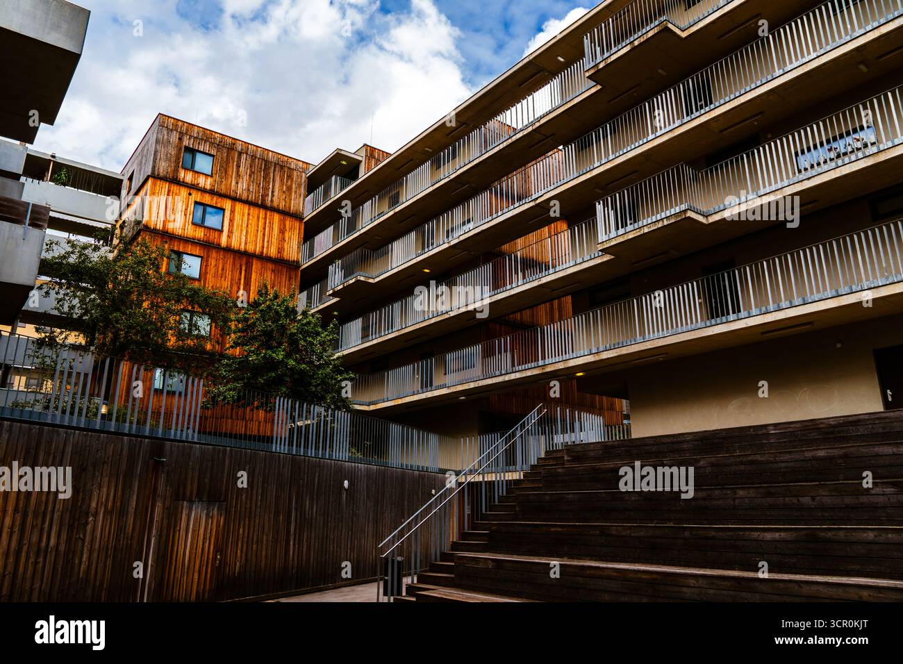 Moderner Wohnkomplex mit Holzfassadenelementen und offenen Balkonen, die eine warme, zeitgenössische Atmosphäre im Innenhof schaffen Stockfoto