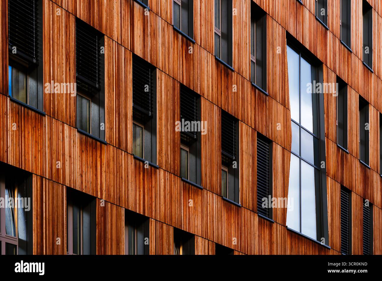 Moderner Wohnkomplex mit Holzfassadenelementen und offenen Balkonen, die eine warme, zeitgenössische Atmosphäre im Innenhof schaffen Stockfoto