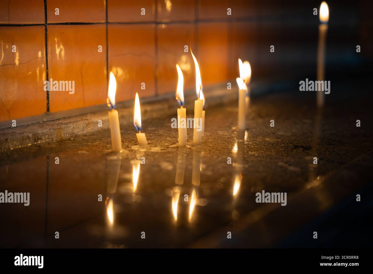 Kerzen brennen in der Kirche, reflektieren auf nasser Oberfläche. Flimmernde Hoffnung im Dunkeln. Leises Licht in stilem Wasser. Gebet und Anbetung Stockfoto