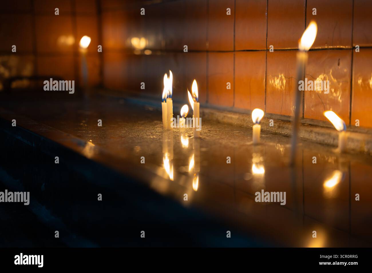 Kerzen brennen in der Kirche, reflektieren auf nasser Oberfläche. Flimmernde Hoffnung im Dunkeln. Leises Licht in stilem Wasser. Gebet und Anbetung Stockfoto