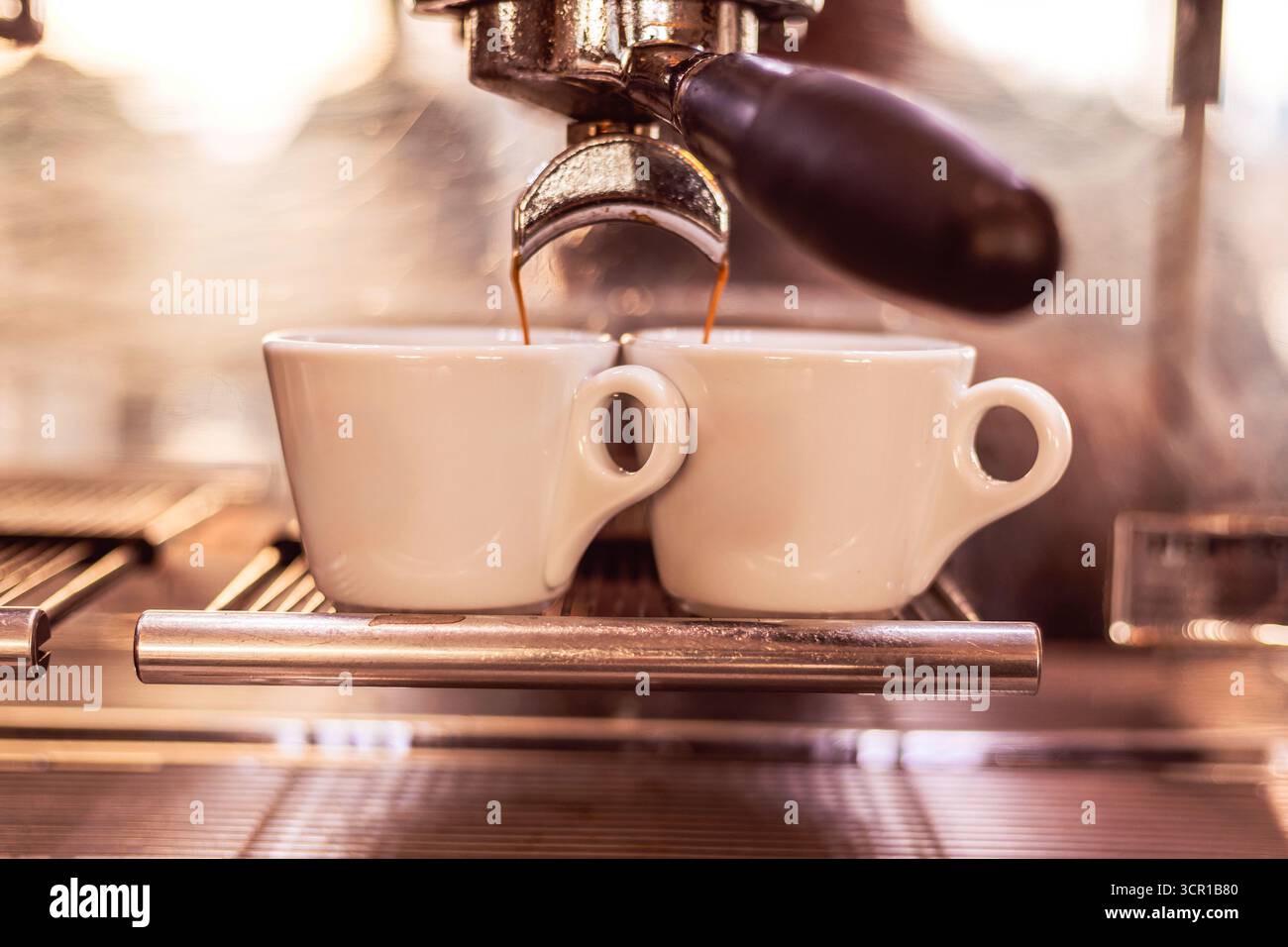 Aus einer glänzenden Espressomaschine in einem belebten Café fließt Kaffee in zwei weiße Espressomaschinen und fängt die lebendige Morgenenergie und das Aroma von Fre ein Stockfoto