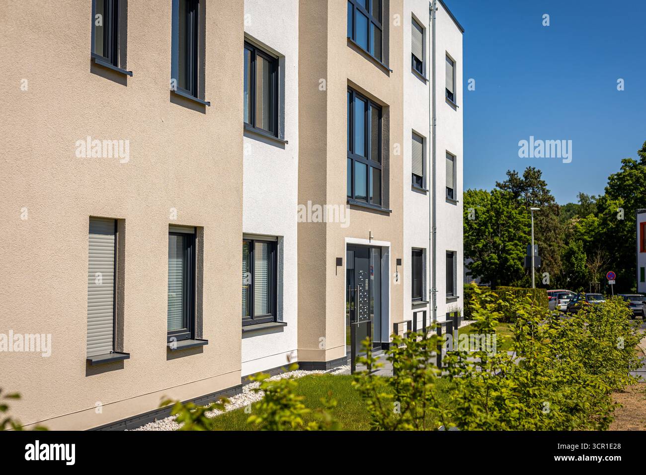 Ein zeitgenössisches Wohngebäude zeigt sein klares Design und helle Farben unter einem klaren blauen Himmel. Gepflegte Landschaftsgestaltung verstärkt die einladende Atmosphäre Stockfoto