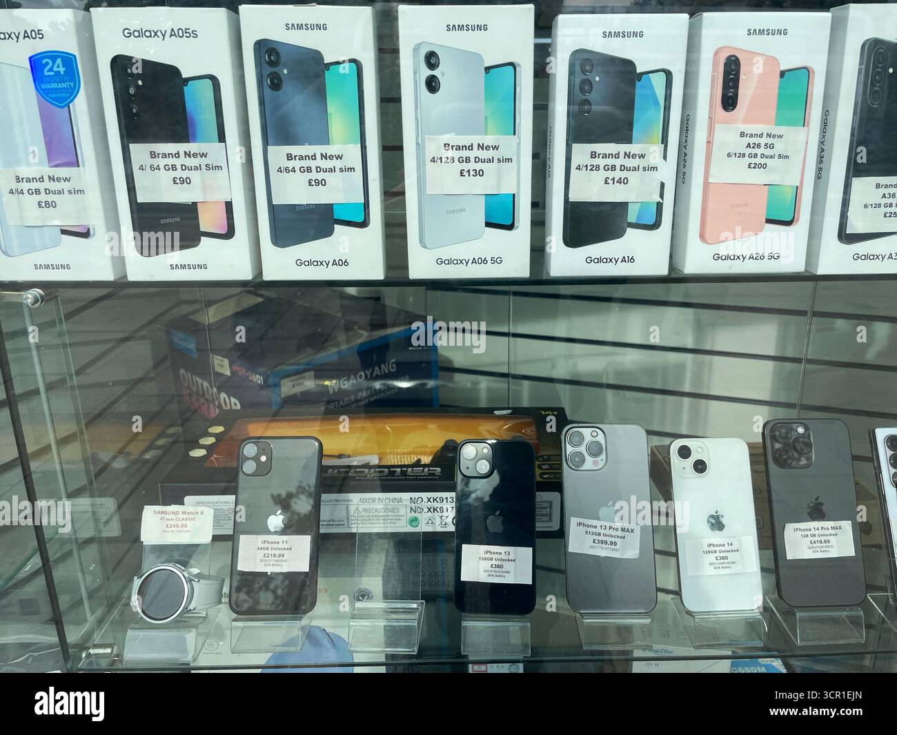 Brandneue und generalüberholte Samsung und iPhone Smartphone-Modelle zum Verkauf in einem Handy-Shop-Fenster - Smartphone-aufgenommenes Stockfoto