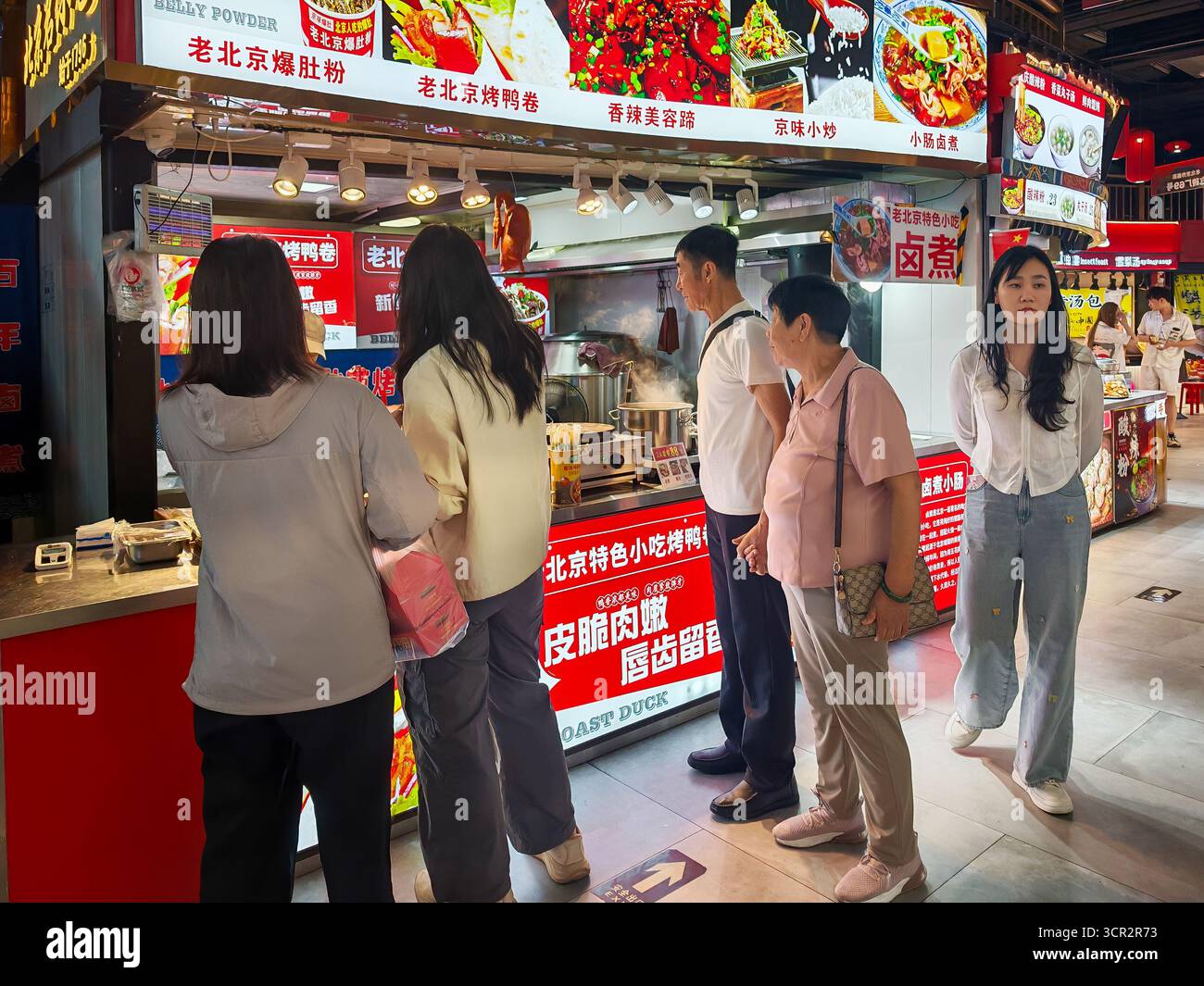 Peking, China - 15. September 2025 : die Leute stehen an einem belebten Imbissstand in Pekings belebter Qianmen-Straße an und genießen köstliche lokale Küche. Stockfoto