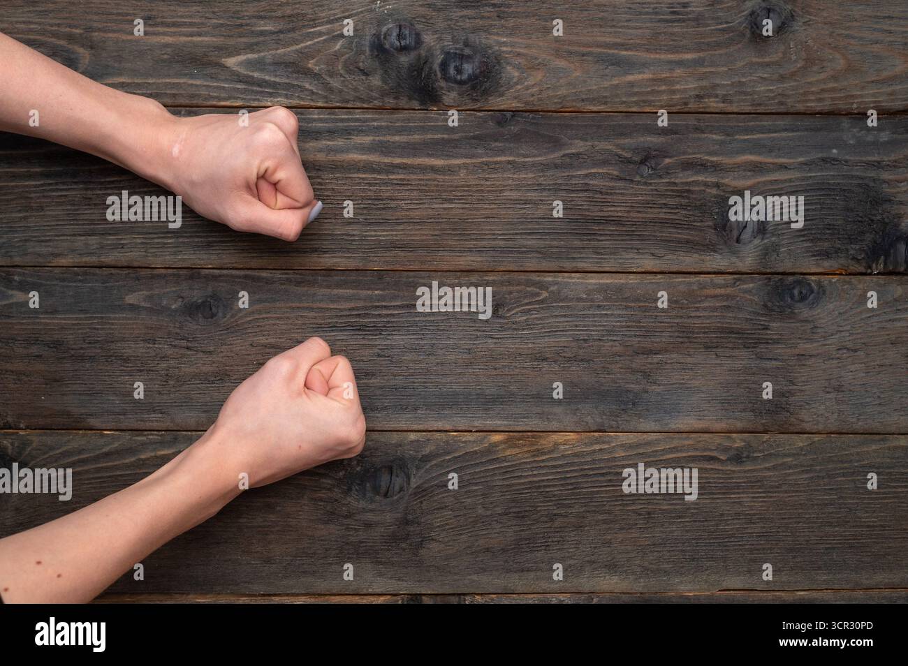 Weibliche Hände geballt in der Faust auf hölzernem Hintergrund, zeigen Stärke und Entschlossenheit. Die Fäuste der Frau liegen auf rustikalem Holztisch, die feste r Stockfoto
