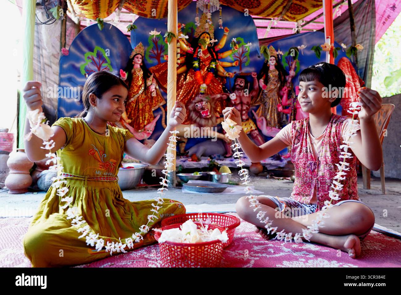 Dhaka, Dhaka, Bangladesch. September 2025. Mit der Ankunft des Herbstes in Bengalen läutet der Duft der Sheuli-Blüten das Aufkommen von Durga Puja ein. Der Rhythmus des Dhak, der Klang der Muschel und die frische Verzierung der Natur schaffen zusammen eine festliche Atmosphäre. Am 29. September 2025, dem Tag von Maha Saptami, konnte man bei der Überquerung von schlammigen Straßen und einer provisorischen Brücke aus Betelnussbäumen eine einzigartige ländliche Feier von Durga Puja im Boral Bari im Dorf Swarupkathi erleben. Mit bunten Blumen, den Takten des Dhak und der anmutigen Teilnahme von Dorffrauen, der Anbetungskredit Stockfoto