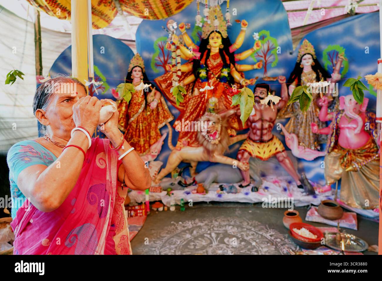 Dhaka, Dhaka, Bangladesch. September 2025. Mit der Ankunft des Herbstes in Bengalen läutet der Duft der Sheuli-Blüten das Aufkommen von Durga Puja ein. Der Rhythmus des Dhak, der Klang der Muschel und die frische Verzierung der Natur schaffen zusammen eine festliche Atmosphäre. Am 29. September 2025, dem Tag von Maha Saptami, konnte man bei der Überquerung von schlammigen Straßen und einer provisorischen Brücke aus Betelnussbäumen eine einzigartige ländliche Feier von Durga Puja im Boral Bari im Dorf Swarupkathi erleben. Mit bunten Blumen, den Takten des Dhak und der anmutigen Teilnahme von Dorffrauen, der Anbetungskredit Stockfoto