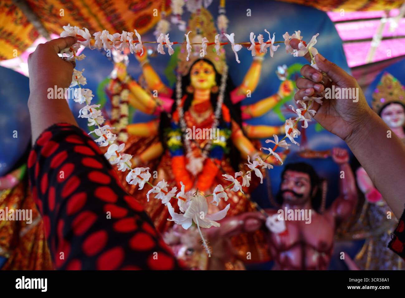 Dhaka, Dhaka, Bangladesch. September 2025. Mit der Ankunft des Herbstes in Bengalen läutet der Duft der Sheuli-Blüten das Aufkommen von Durga Puja ein. Der Rhythmus des Dhak, der Klang der Muschel und die frische Verzierung der Natur schaffen zusammen eine festliche Atmosphäre. Am 29. September 2025, dem Tag von Maha Saptami, konnte man bei der Überquerung von schlammigen Straßen und einer provisorischen Brücke aus Betelnussbäumen eine einzigartige ländliche Feier von Durga Puja im Boral Bari im Dorf Swarupkathi erleben. Mit bunten Blumen, den Takten des Dhak und der anmutigen Teilnahme von Dorffrauen, der Anbetungskredit Stockfoto