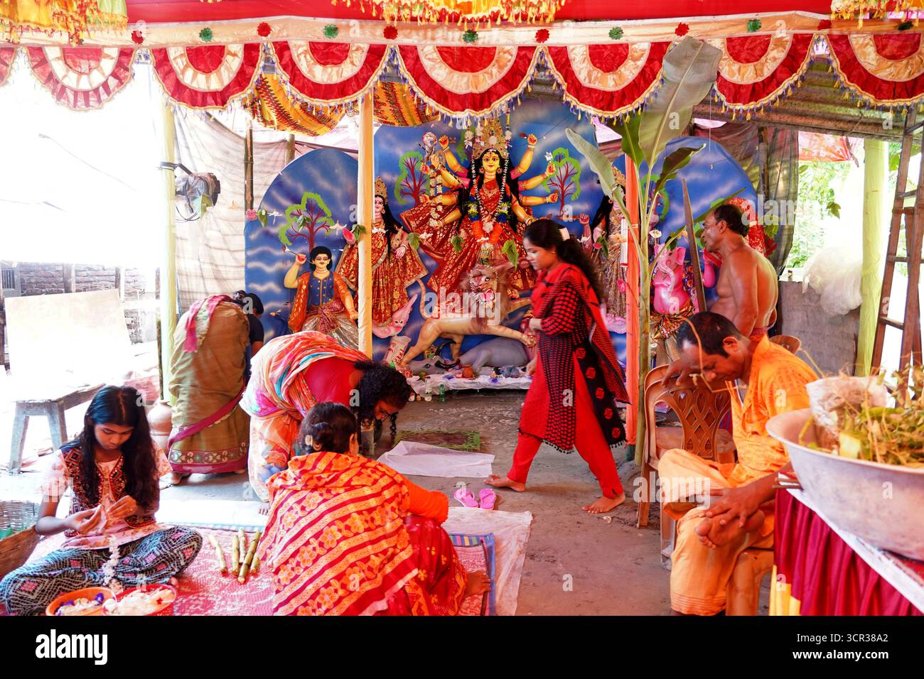 Dhaka, Dhaka, Bangladesch. September 2025. Mit der Ankunft des Herbstes in Bengalen läutet der Duft der Sheuli-Blüten das Aufkommen von Durga Puja ein. Der Rhythmus des Dhak, der Klang der Muschel und die frische Verzierung der Natur schaffen zusammen eine festliche Atmosphäre. Am 29. September 2025, dem Tag von Maha Saptami, konnte man bei der Überquerung von schlammigen Straßen und einer provisorischen Brücke aus Betelnussbäumen eine einzigartige ländliche Feier von Durga Puja im Boral Bari im Dorf Swarupkathi erleben. Mit bunten Blumen, den Takten des Dhak und der anmutigen Teilnahme von Dorffrauen, der Anbetungskredit Stockfoto