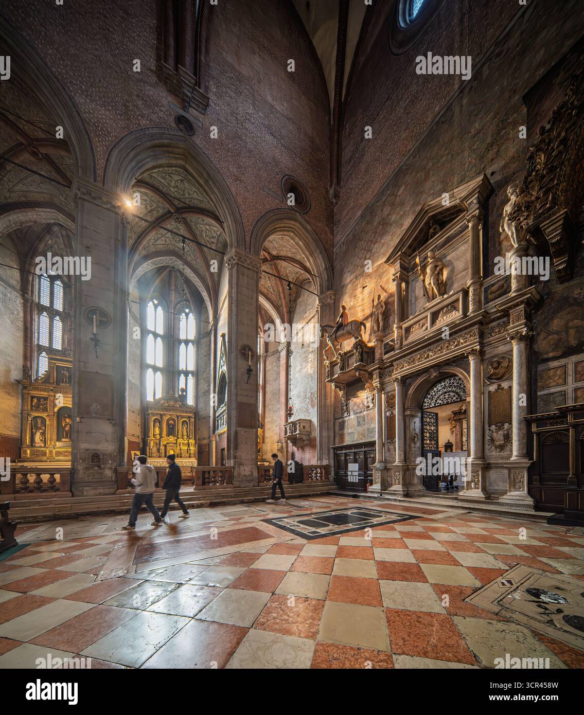 Sakristentor und Apsiskapellen in Santa Maria dei Frari, Venedig. Geschnitzter Stein und vergoldete Altäre leuchten unter geriffelten Gewölben und gefiltertem Licht. Stockfoto