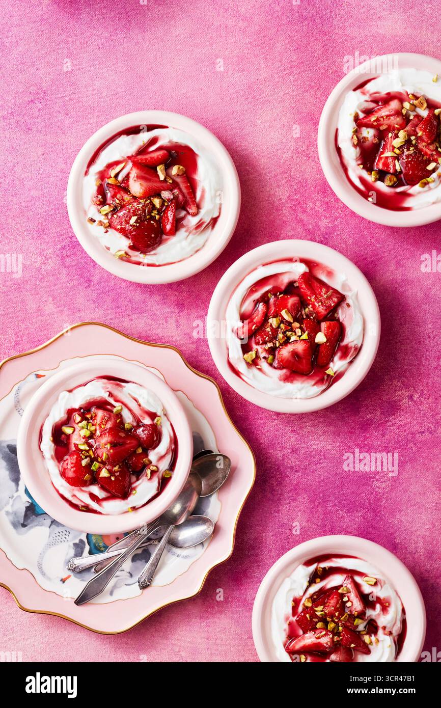Desserts aus Erdbeeren und Creme in rosafarbenen Schüsseln, elegant auf einer strukturierten rosa Oberfläche angeordnet. Stockfoto