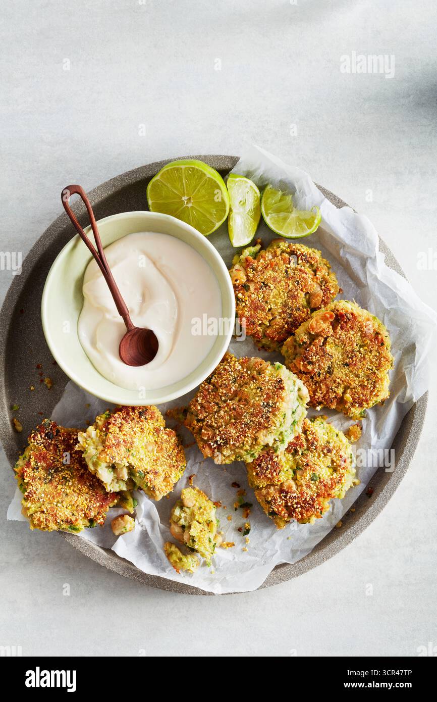 Knusprige Falafelfritter mit Joghurt-Dip und Limettenscheiben auf einem mit Pergament gefütterten Teller. Stockfoto