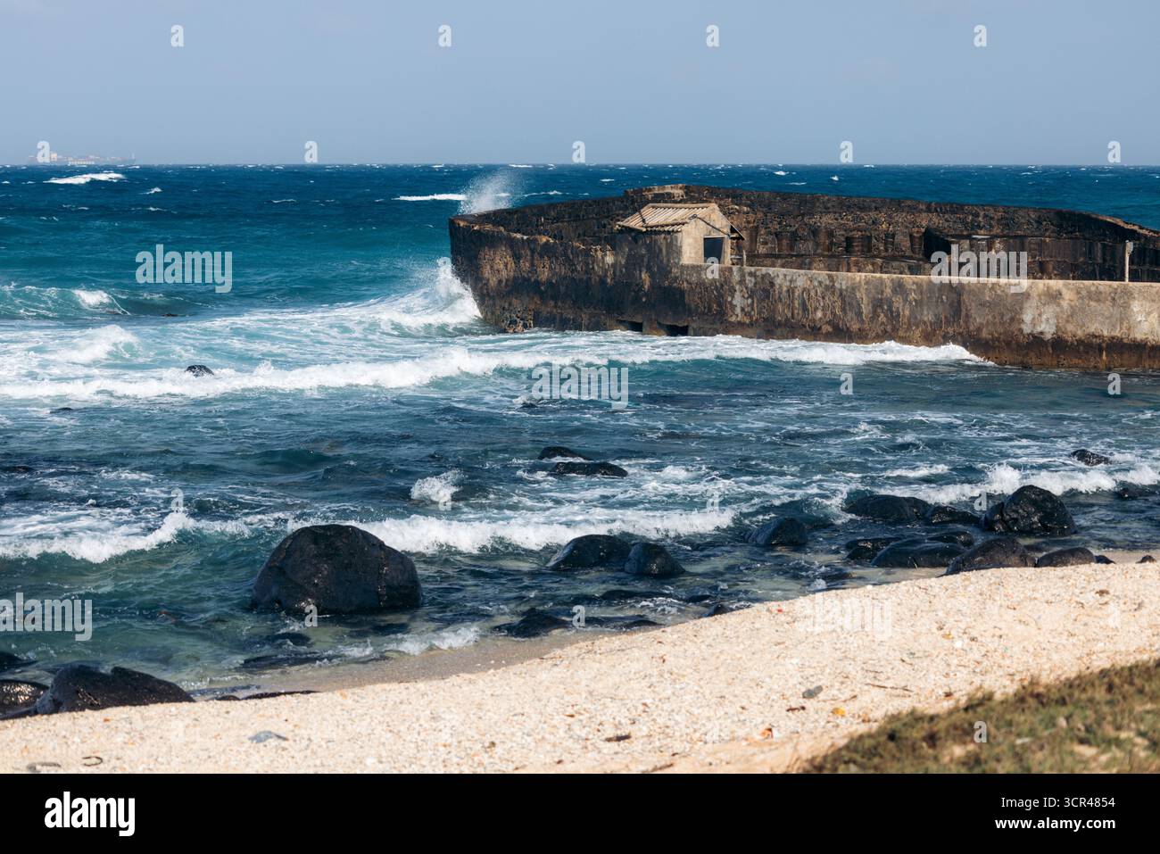Die Wellen stürzen gegen einen zerklüfteten Steinsteg unter einem klaren blauen Himmel. Phu Quy Island, Bnh Thuan, Vietnam Stockfoto