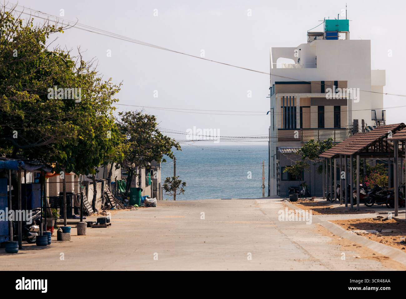 Blick auf die Küstenstraße mit einem modernen weißen Gebäude und entfernter Meereskulisse. Phu Quy Island, Bnh Thuan, Vietnam Stockfoto