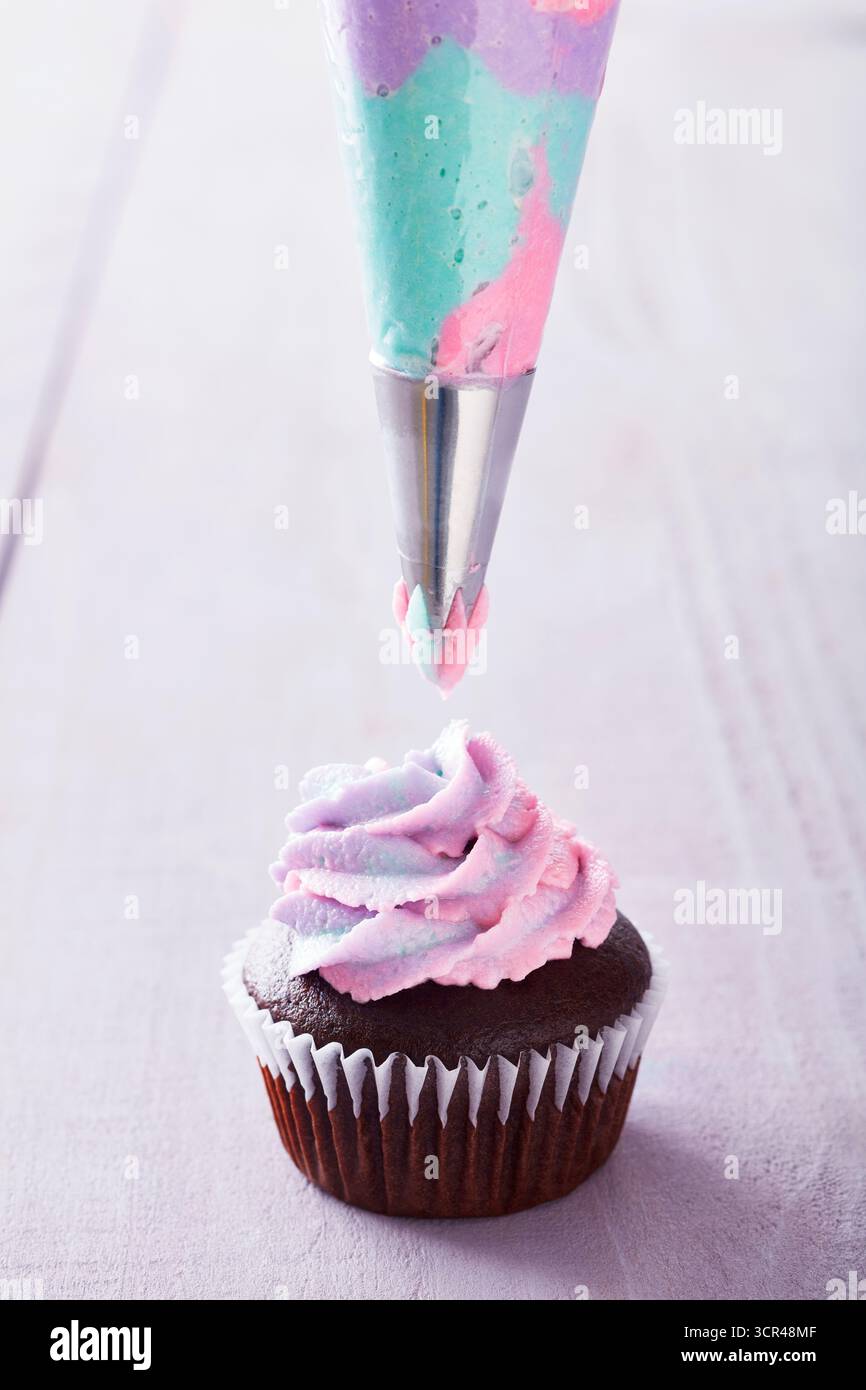 Schokoladen-Cupcake mit pinkfarbenen, lila und blauen Zuckerguss. Stockfoto