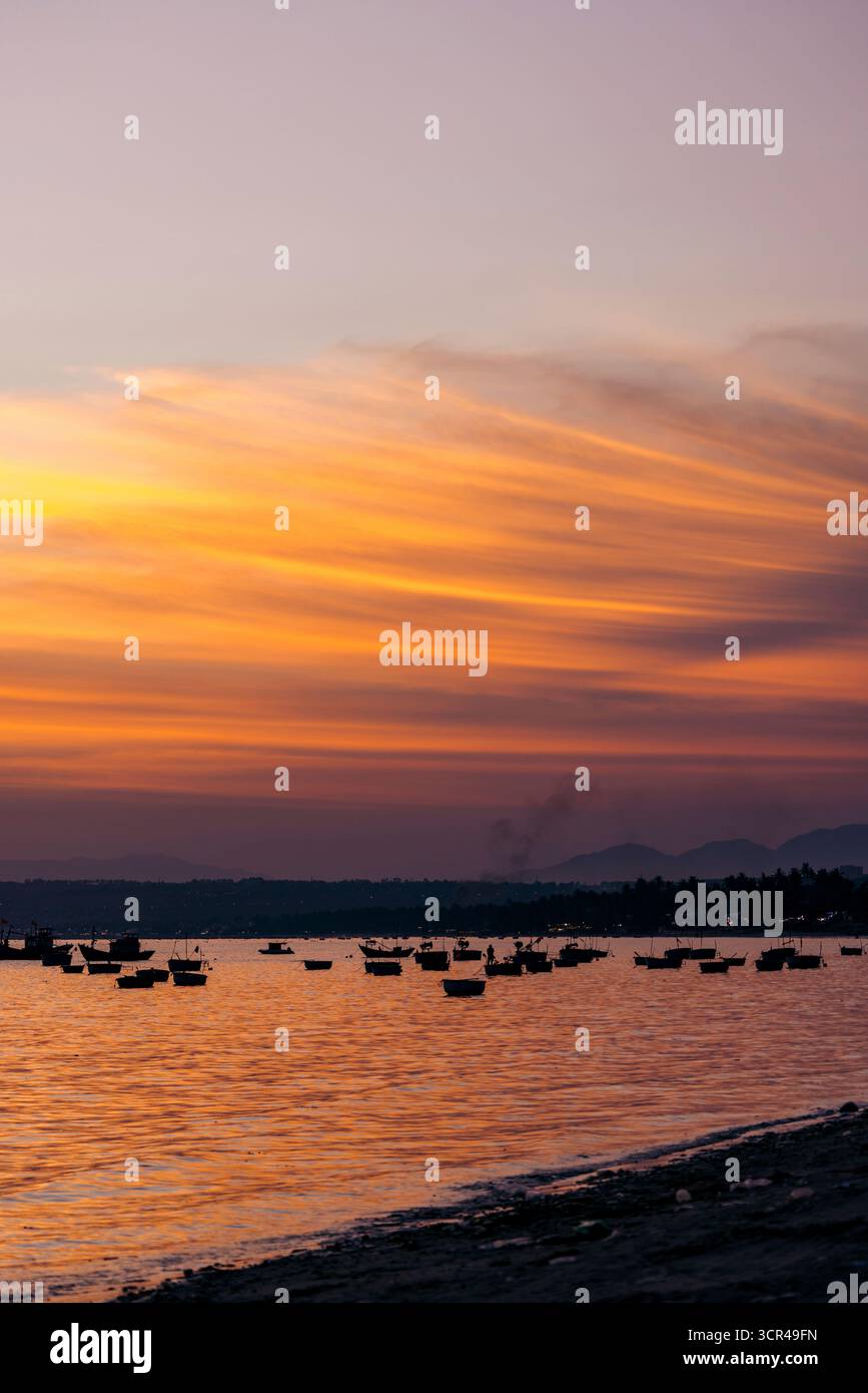 Dramatischer Sonnenuntergang über einem ruhigen See mit Silhouettenbooten und lebendigem Himmel. Mui Ne, Vietnam Mui Ne, Vietnam Stockfoto
