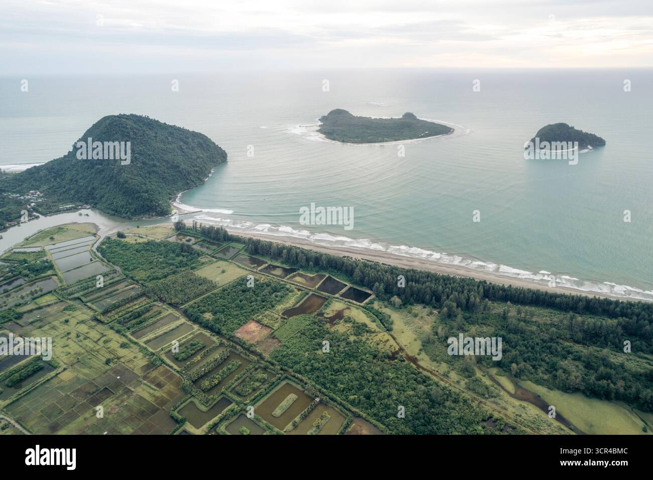 Blick aus der Vogelperspektive auf grünes Ackerland, Wald und Meer mit kleinen Inseln in der Ferne. Aceh Jaya Regency, Aceh, Sumatra, Indonesien Stockfoto