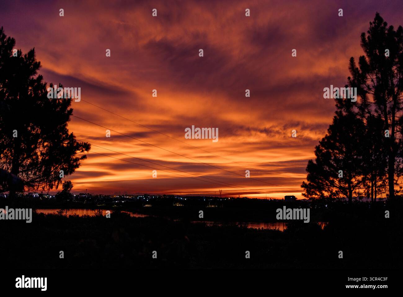 Lebendiger Sonnenuntergangshimmel mit Silhouettenbäumen und einem ruhigen Gewässer. Bao Loc, Vietnam Stockfoto