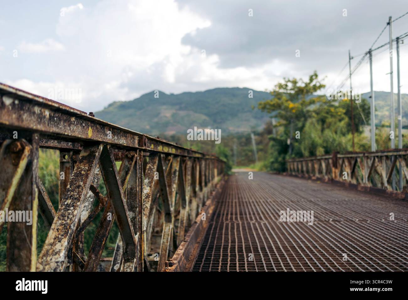 Eine rostige Metallbrücke mit Bergen unter einem bewölkten Himmel im Hintergrund. Bao Loc, Vietnam. Stockfoto