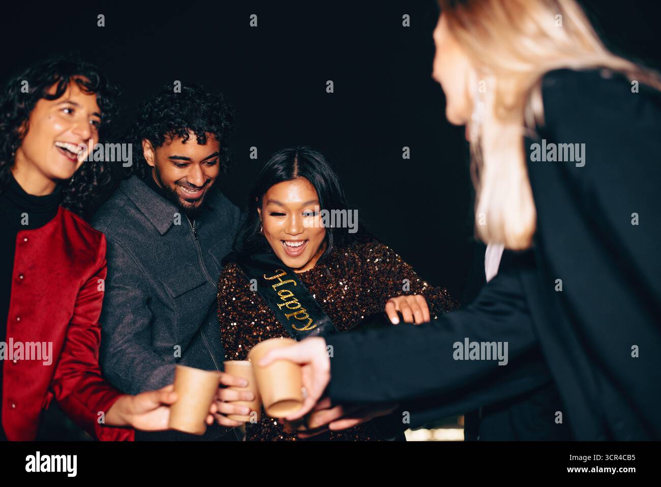 Eine fröhliche Geburtstagsfeier, während das Geburtstagskind Drinks für ihre Freunde schenkt, umgeben von Lachen, Anfeuern und festlicher Partyenergie. Stockfoto