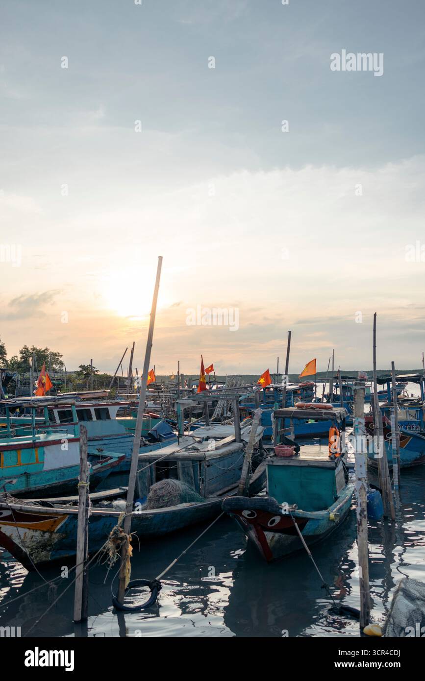 Ein ruhiger Blick auf farbenfrohe Fischerboote, die unter einem ruhigen Abendhimmel mit untergehender Sonne angedockt sind. Thanh Anh, Can Gio, Ho Chi Minh, Vietnam Stockfoto