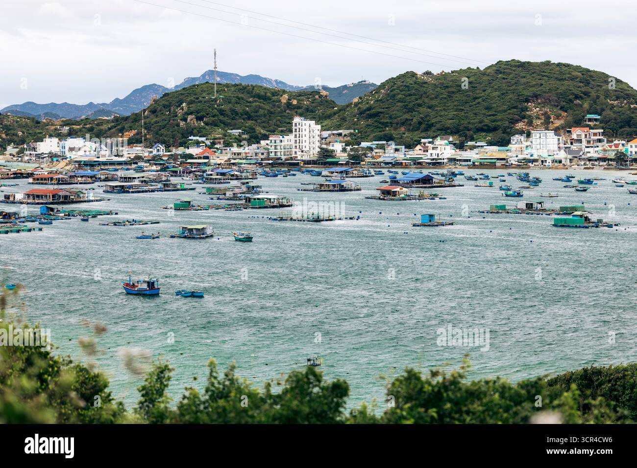 Ein Küstendorf mit schwimmenden Häusern auf dem Wasser, umgeben von grünen Hügeln und fernen Bergen. Ninh Hai District in Ninh Thuan, Vietnam Stockfoto