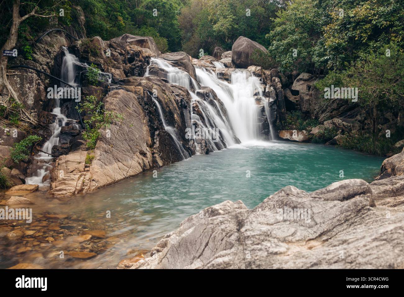Der kaskadierende Nuoc Ngot Wasserfall fließt in einen ruhigen türkisfarbenen Pool, der von üppig grünem Laub umgeben ist. Ninh Thuan, Vietnam Stockfoto