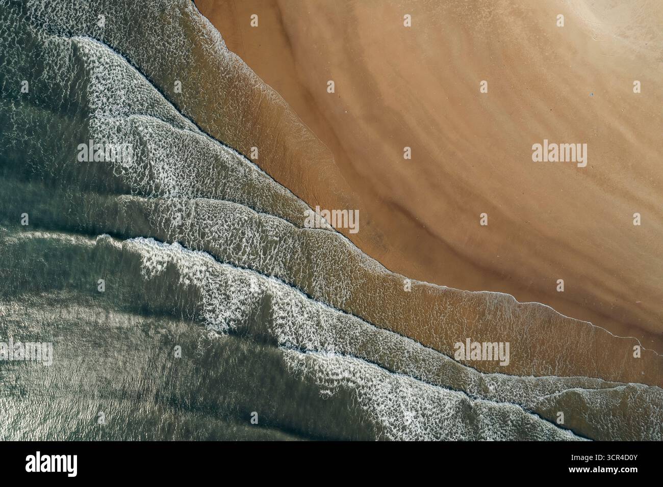 Aus der Vogelperspektive auf Meereswellen, die sanft auf einen glatten Sandstrand stürzen. Ke Ga, Binh Thuan, Vietnam Stockfoto