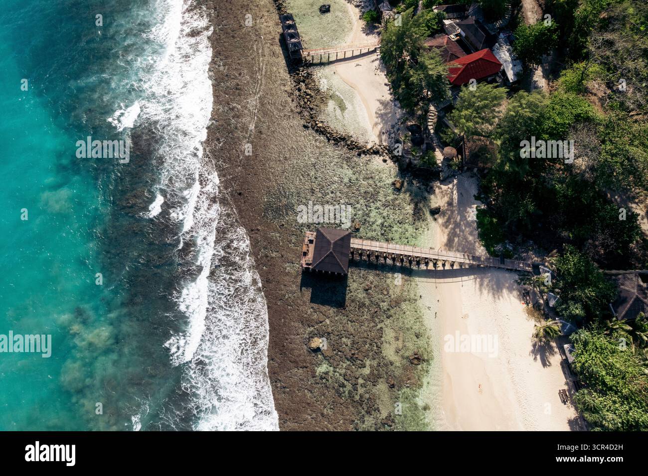 Blick aus der Vogelperspektive auf einen tropischen Strand mit einem Pier, der sich in türkisfarbenes Meer erstreckt. Momong Lampuuk ein Strand in Aceh, Sumatra, Indonesien Stockfoto