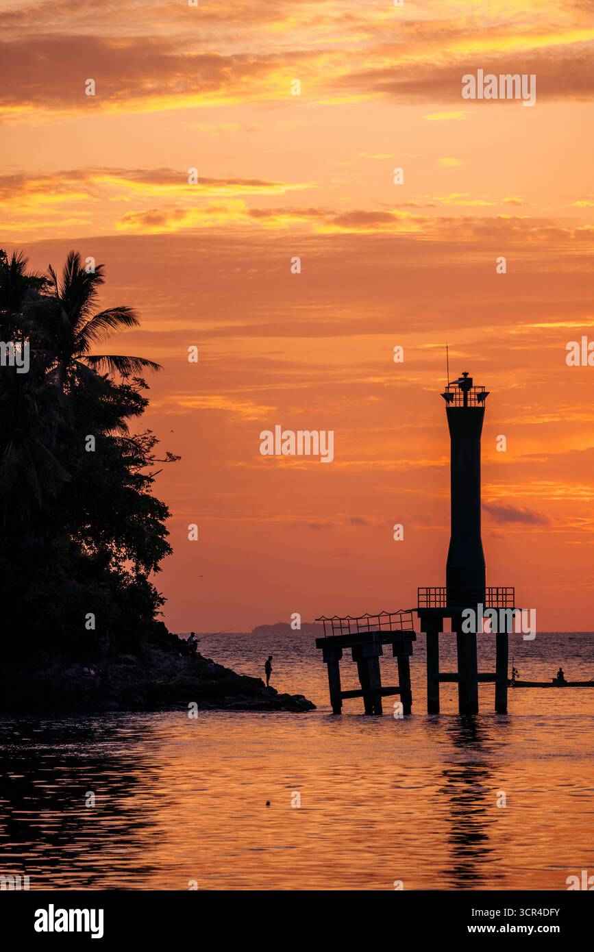 Silhouette eines Leuchtturms bei Sonnenuntergang mit ruhigem Wasser und tropischem Laub. Padang, West Sumatra, Indonesien Stockfoto